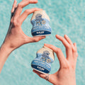 Two Vanilla Sweet Cream Flāv dirty soda mix-in bottles held over a swimming pool